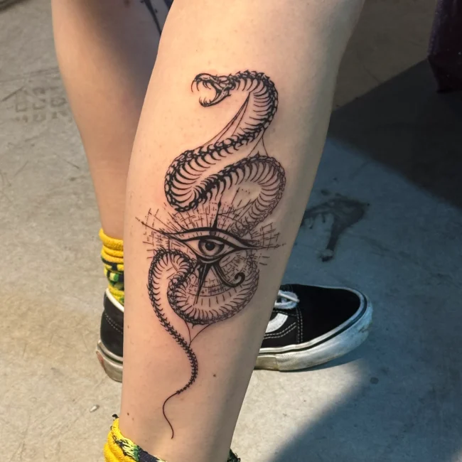 Egyptian-inspired snake tattoo wrapped around the Eye of Horus, created in a detailed black and gray fine line style on the calf.